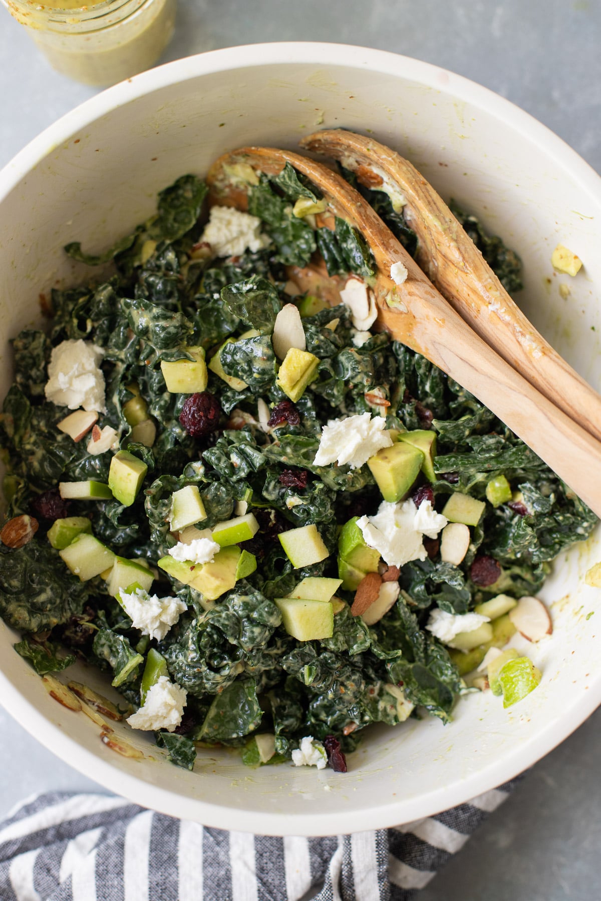 Summer Kale Salad tossed together in a big white bowl with salad tongs off to the side