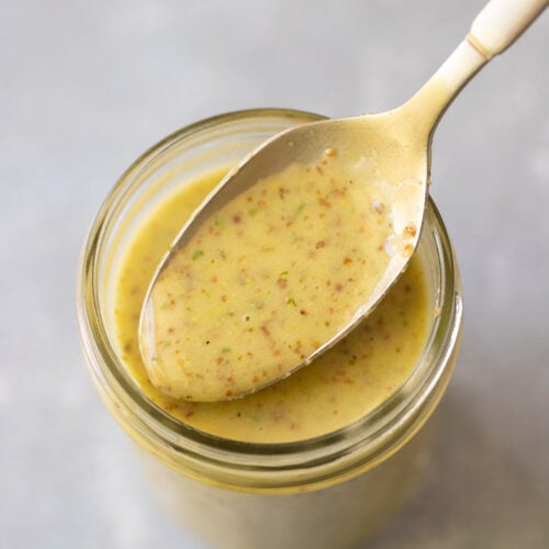 The Best Honey Lemon Dressing in a glass bottle with a spoon taking a scoop out of it