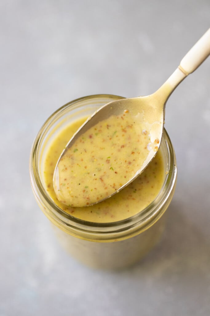 The Best Honey Lemon Dressing in a glass bottle with a spoon taking a scoop out of it