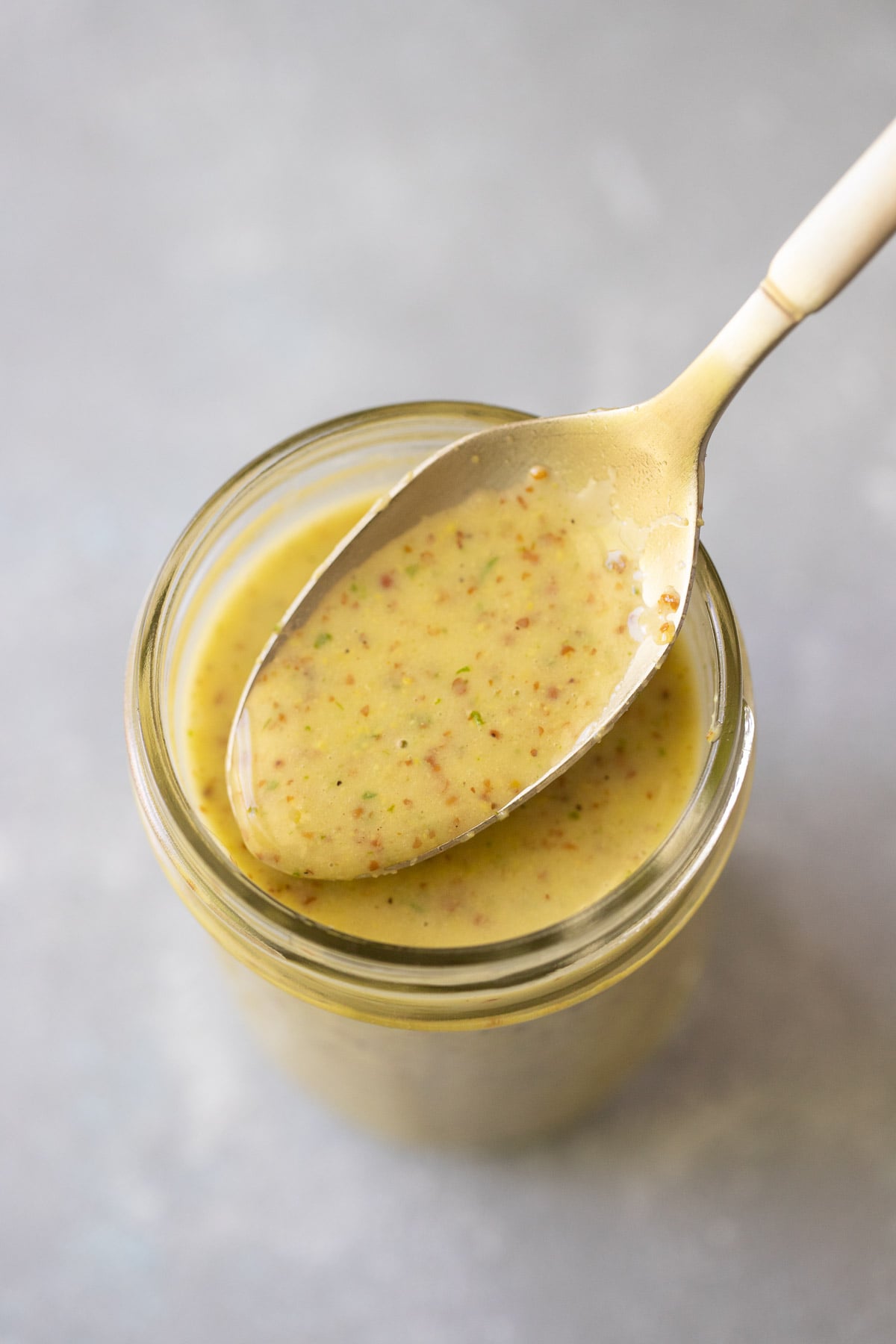 A spoonful of lemon Dijon dressing being held over a mason jar holding more of the homemade vinaigrette.