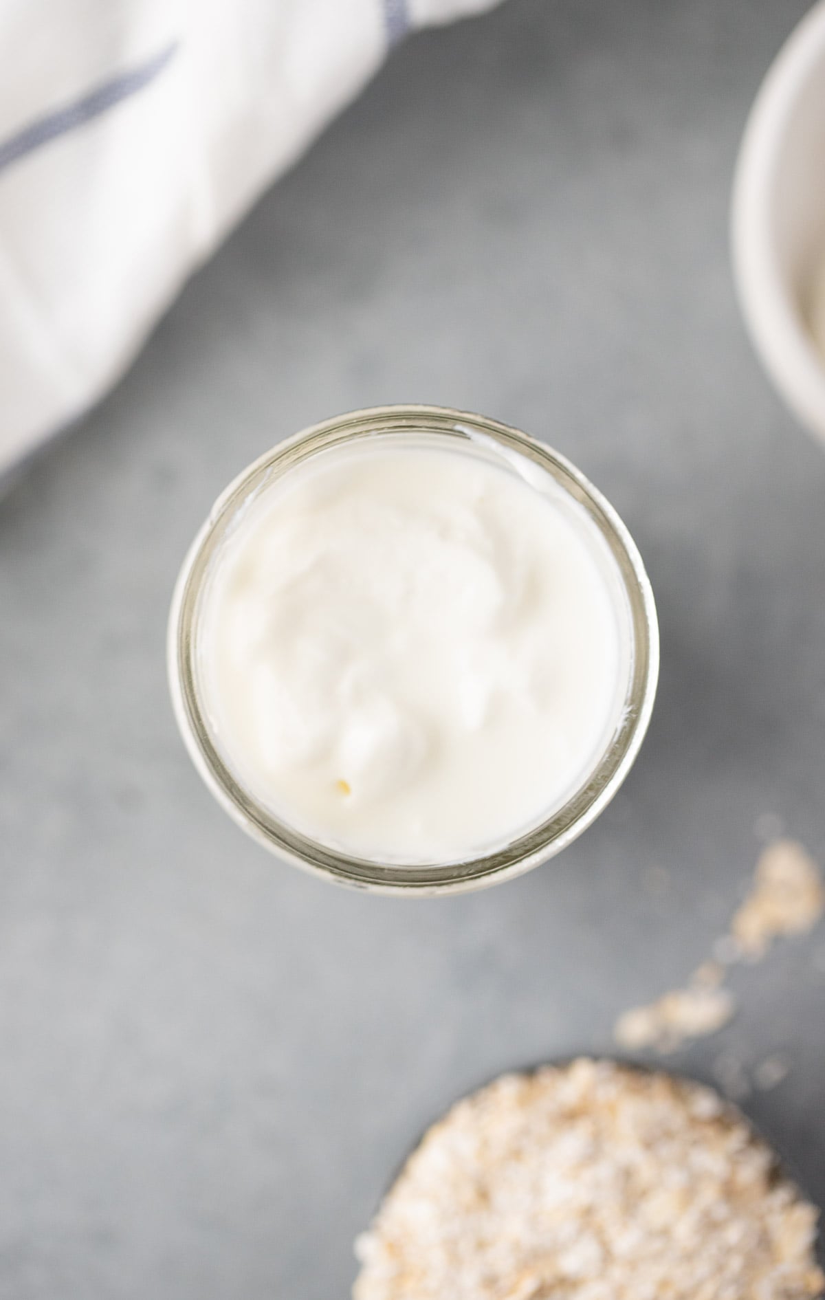 An overhead shot of a mason jar filled with overnight oats being prepared for mango overnight oats on a grey background