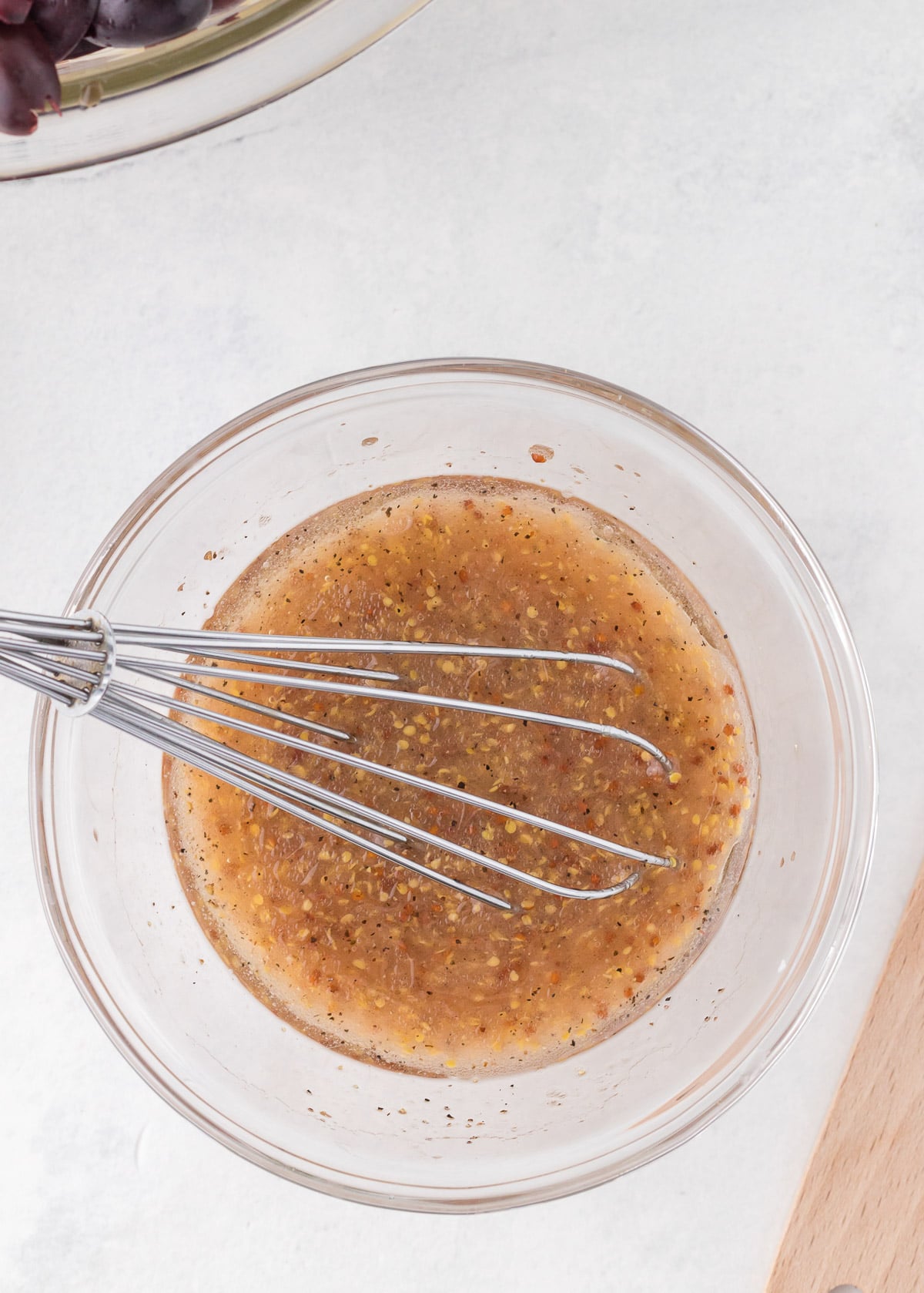 Dressing for greek orzo salad in a clear bowl after being whisked with a whisk in the bowl