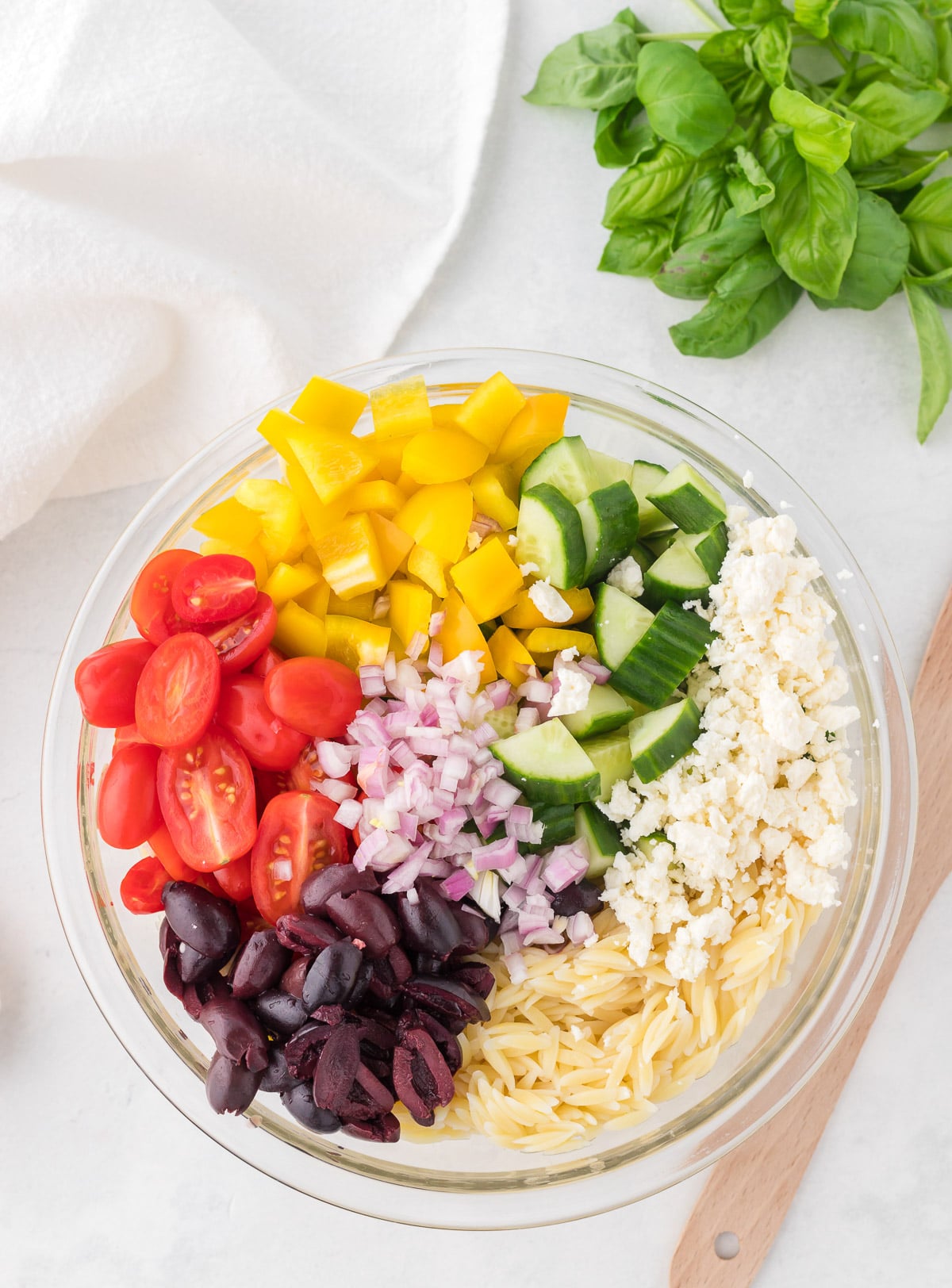 Ingredients for orzo salad in a clear bowl before being mixed