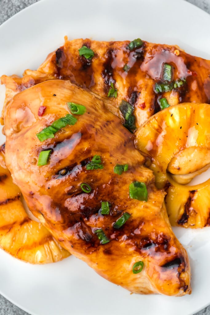 Pineapple grilled chicken on a white plate with green onions on top
