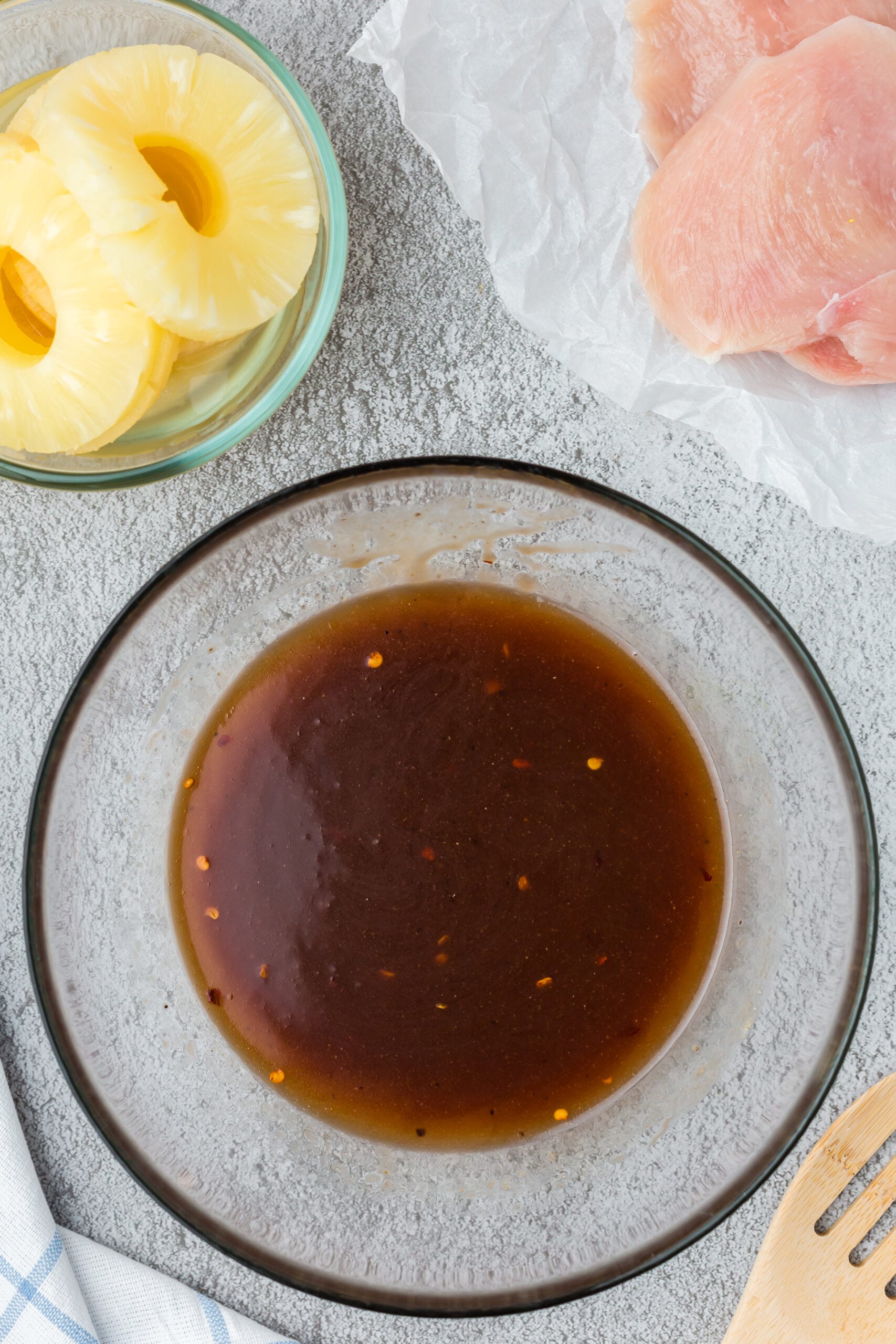 marinade for pineapple grilled chicken in a clear bowl with pineapple and raw chicken breasts on the side