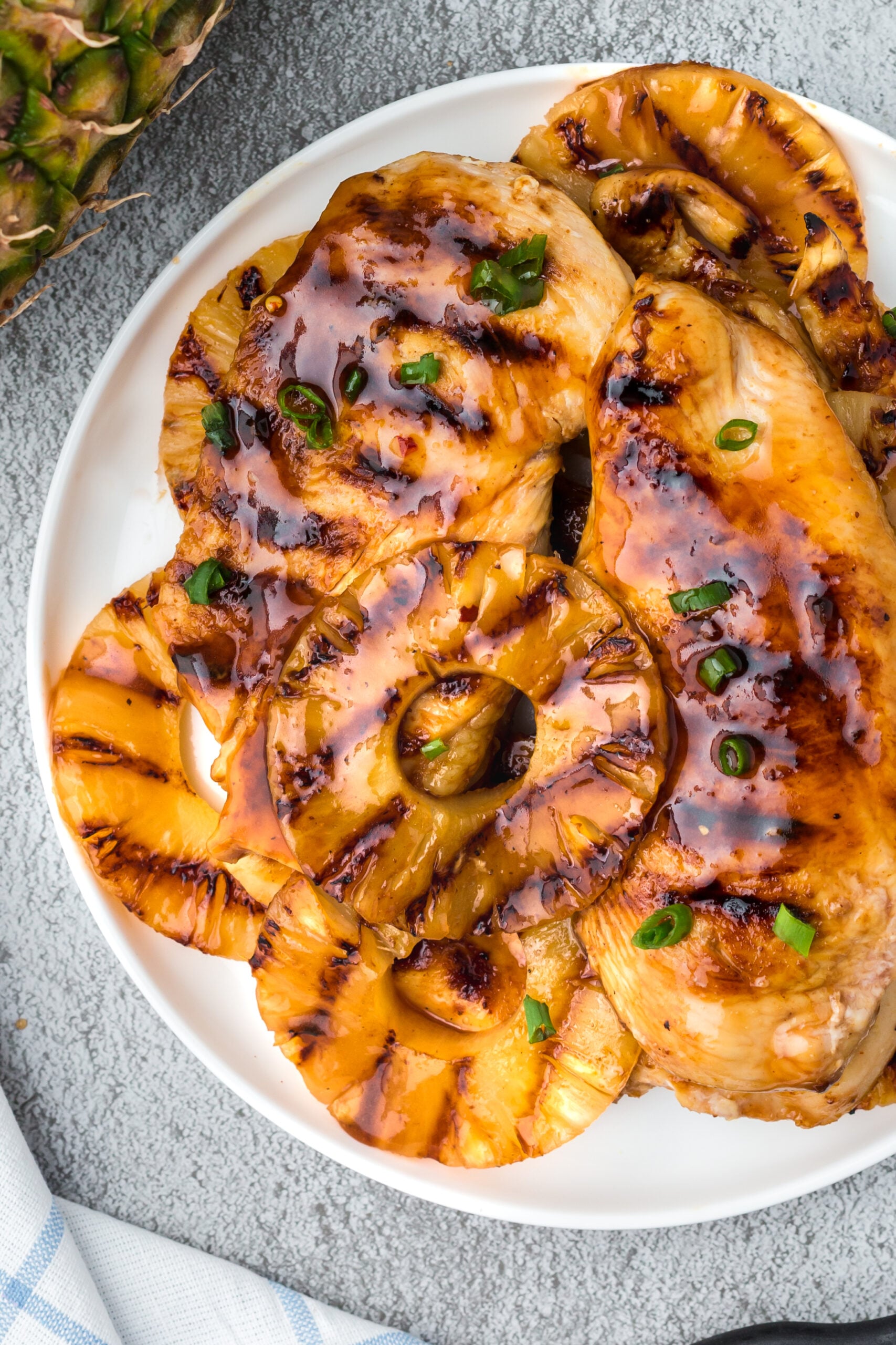 Pineapple grilled chicken on a white plate with green onions on top and a pineapple on the side