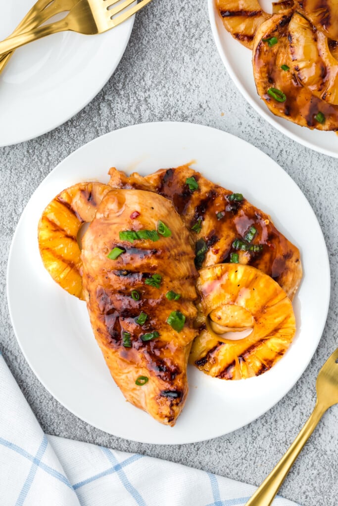 Pineapple grilled chicken on a white plate with green onions on top on a grey background with more plates on the side