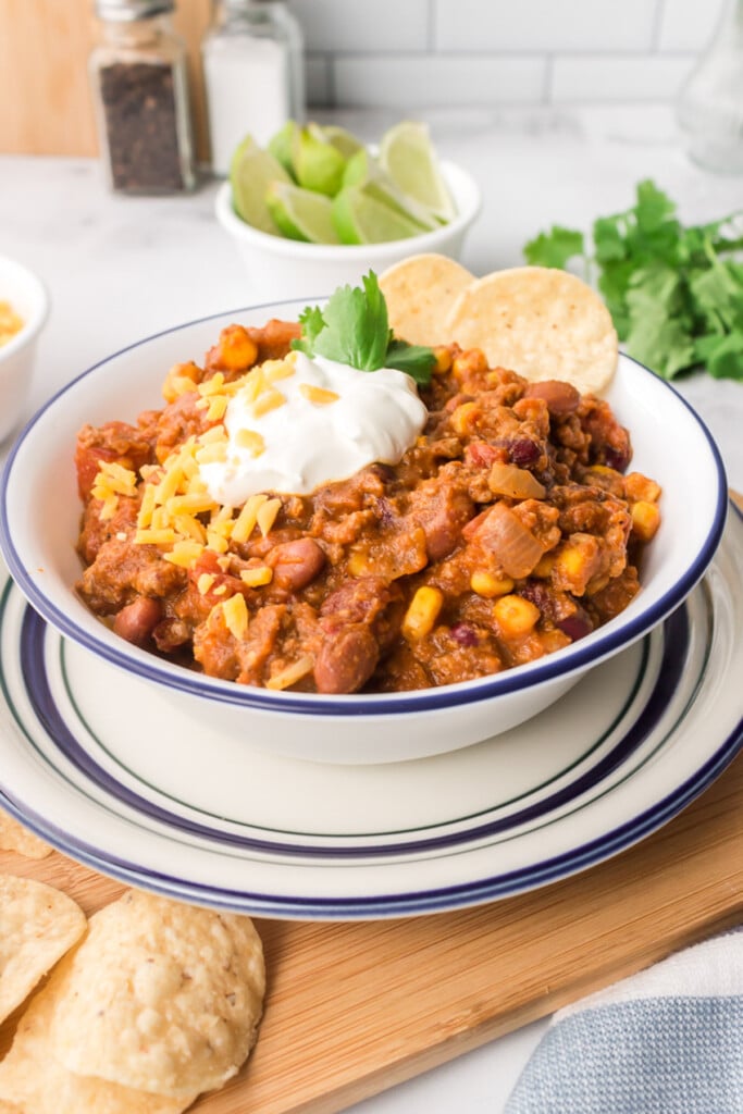 A white bowl of pumpkin chili with sour cream and tortilla chips on the side with limes in the background