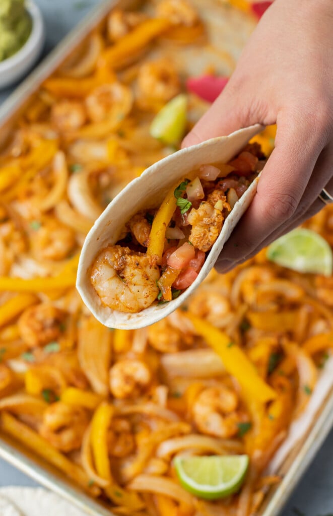 A close up of a hand holding a shrimp fajita taco in flour tortillas 