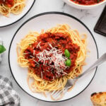 An overhead shot of a white plate of pasta with healthy turkey bolognese and a bowl of the bolognese on the side