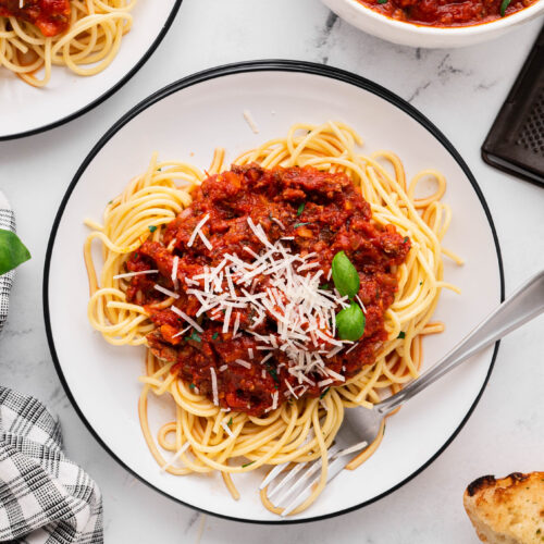 An overhead shot of a white plate of pasta with healthy turkey bolognese and a bowl of the bolognese on the side