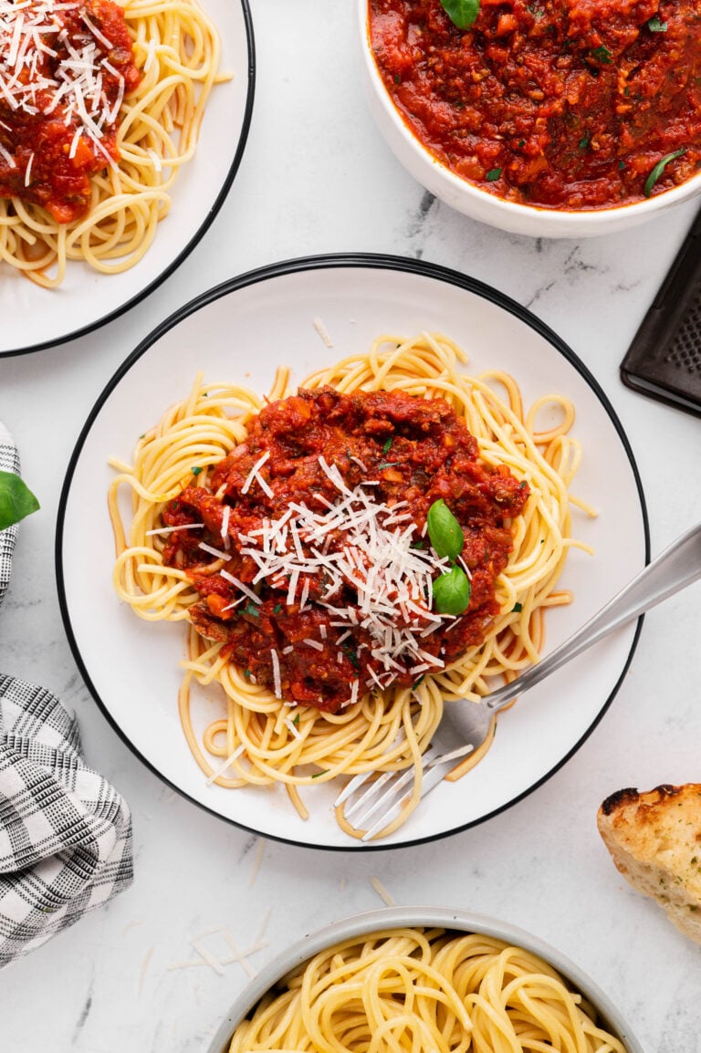 An overhead shot of a white plate of pasta with healthy turkey bolognese and a bowl of the bolognese on the side