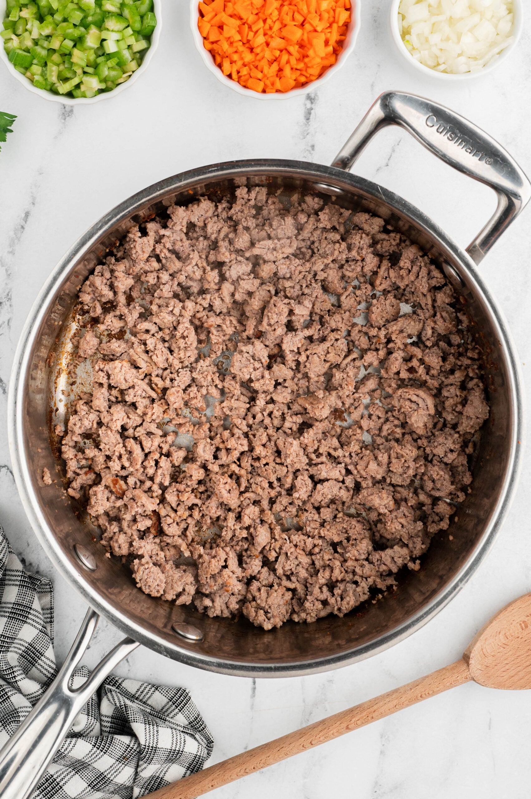 Browned ground turkey in a pan for healthy turkey bolognese with bowls of chopped veggies on the side