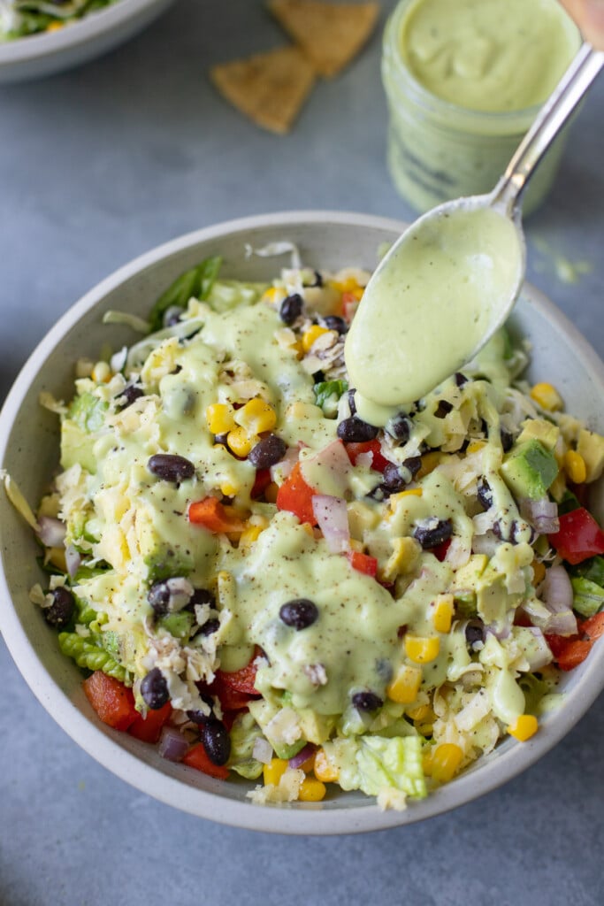 a close up of a salad being drizzled with avocado ranch dressing