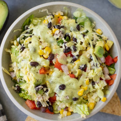A close up of avocado ranch salad in a white bowl on a grey background