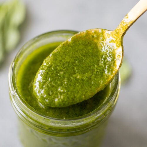 A close up of a spoon scooping out basil dressing from a mason jar