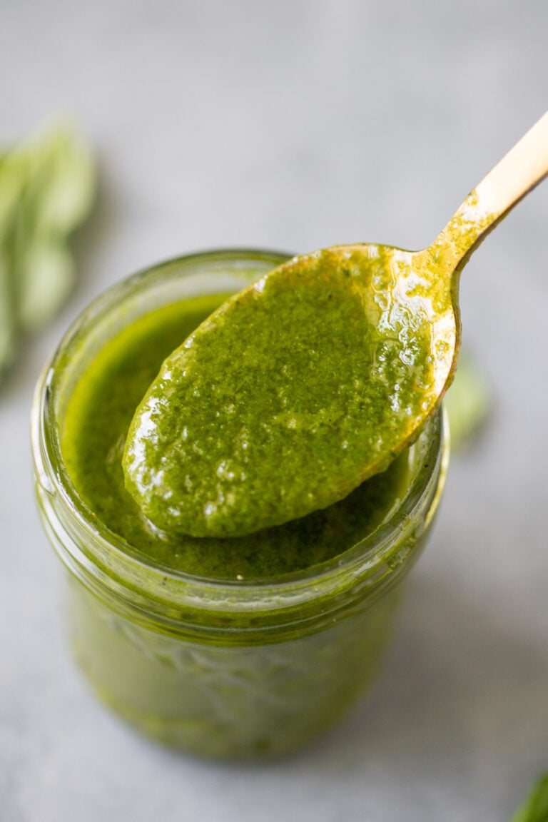 A close up of a spoon scooping out basil dressing from a mason jar