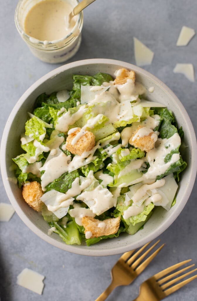 A close up of healthy caesar salad on a grey background with healthy dressing off to the side