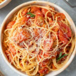 An overhead shot of spaghetti sauce with fresh tomatoes over spaghetti noodles and cheese on a grey background