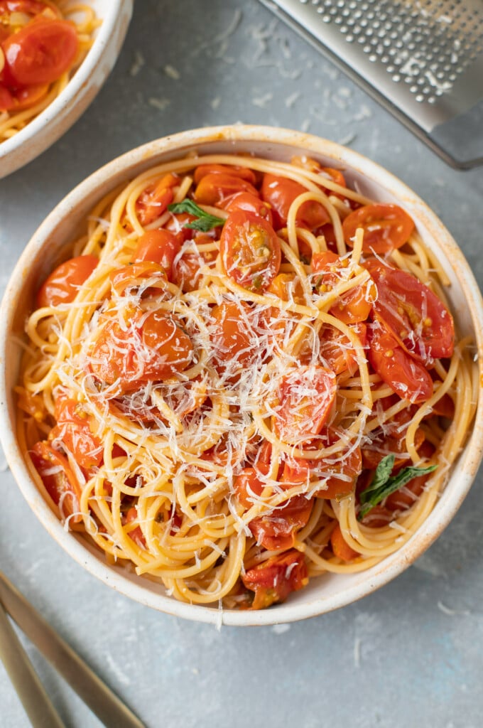 An overhead shot of cherry tomato sauce with fresh tomatoes over spaghetti noodles and cheese on a grey background