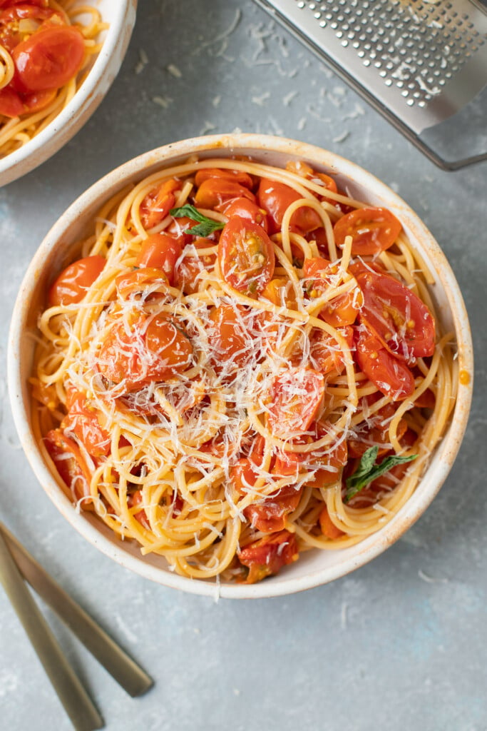 An overhead shot of cherry tomato pasta sauce over spaghetti noodles and cheese on a grey background