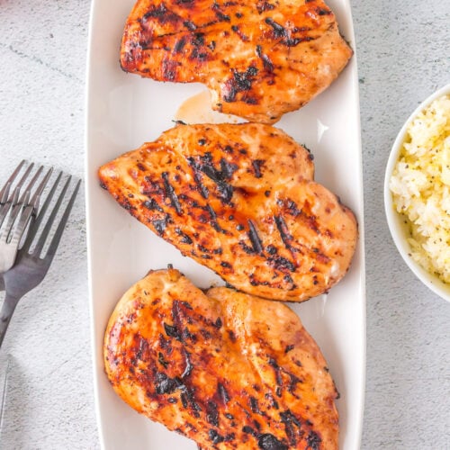 An overhead shot of three grilled teriyaki chicken breasts on a white plate