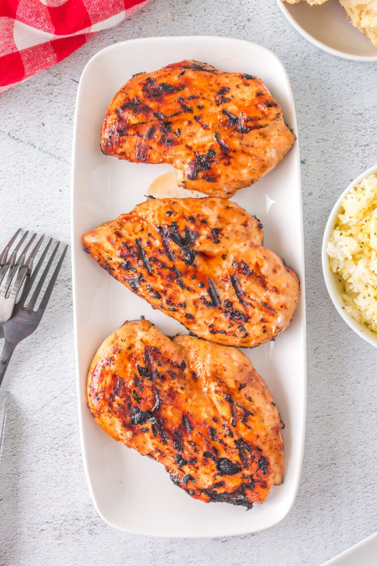 An overhead shot of three grilled teriyaki chicken breasts on a white plate