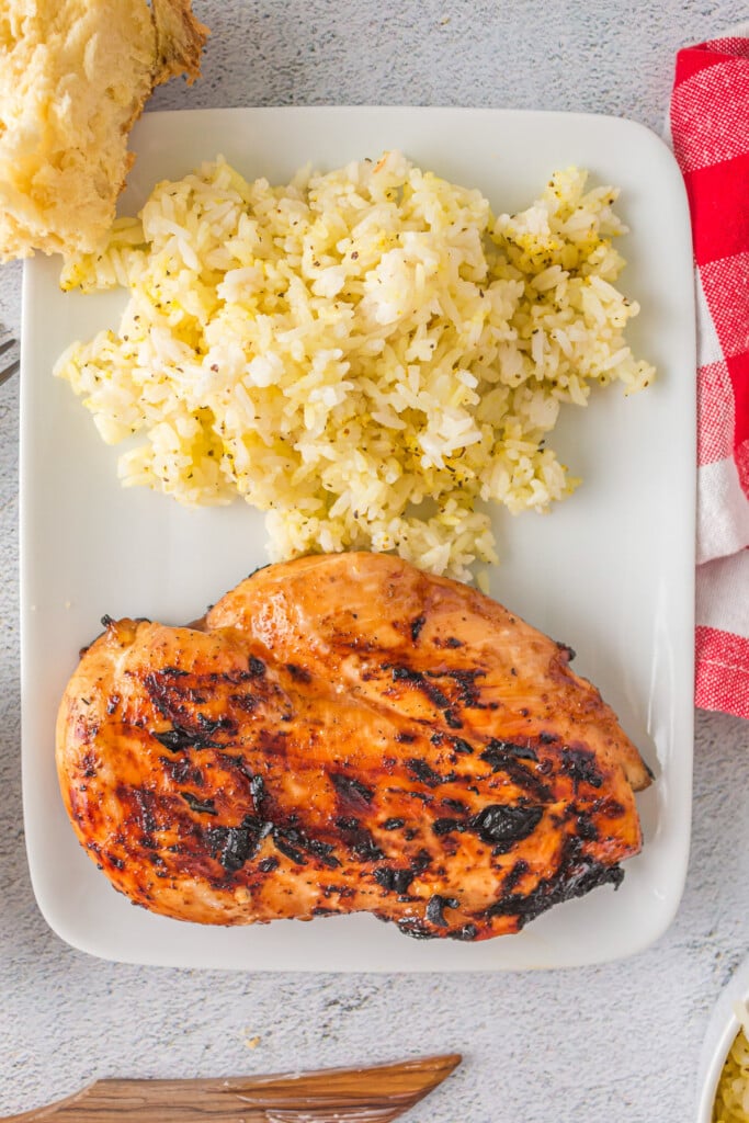 An overhead shot of a grilled teriyaki chicken breast with rice on a white plate