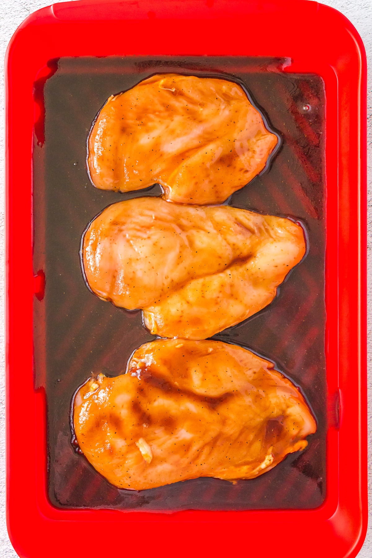 Raw chicken breast marinating in homemade teriyaki sauce in a red tray