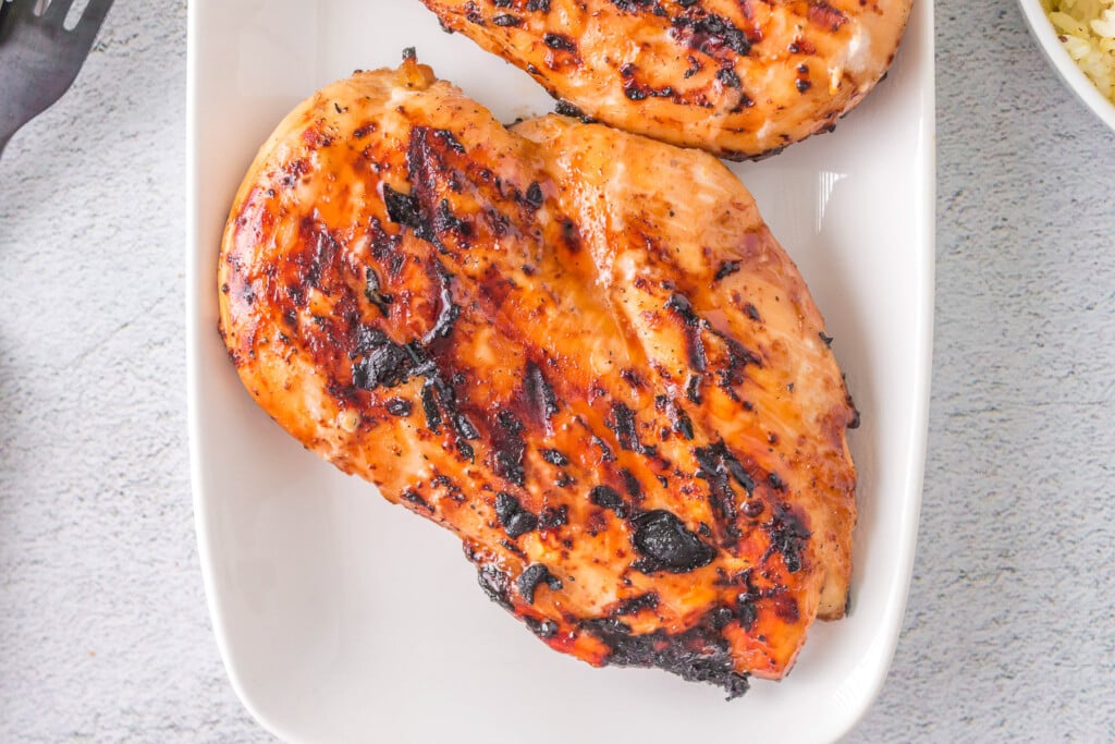 A grilled teriyaki chicken breast on a white plate