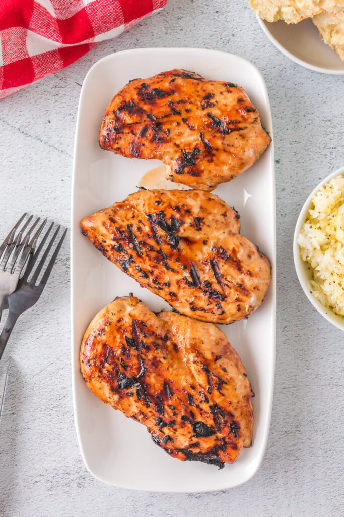 An overhead shot of three grilled teriyaki chicken breasts on a white plate