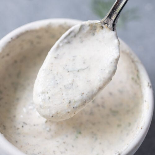 a spoon scooping up greek yogurt ranch dressing from a white bowl