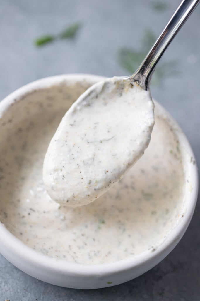 a spoon scooping up greek yogurt ranch dressing from a white bowl
