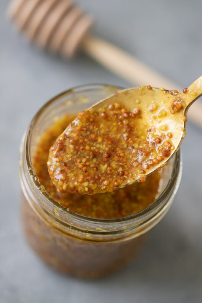 A close up of a spoon of honey mustard dressing being scooped out of a mason jar