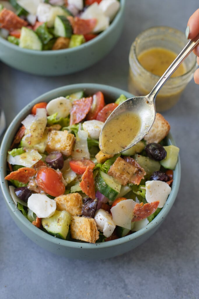 A close up of italian salad with homemade italian dressing being drizzled on top of it