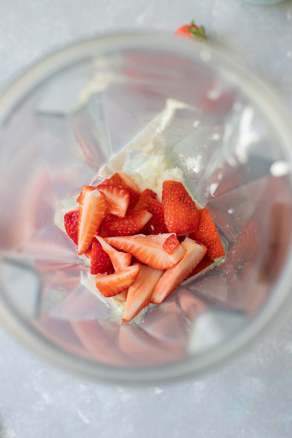 An overhead shot of ingredients for smoothie with strawberries in a blender before blending