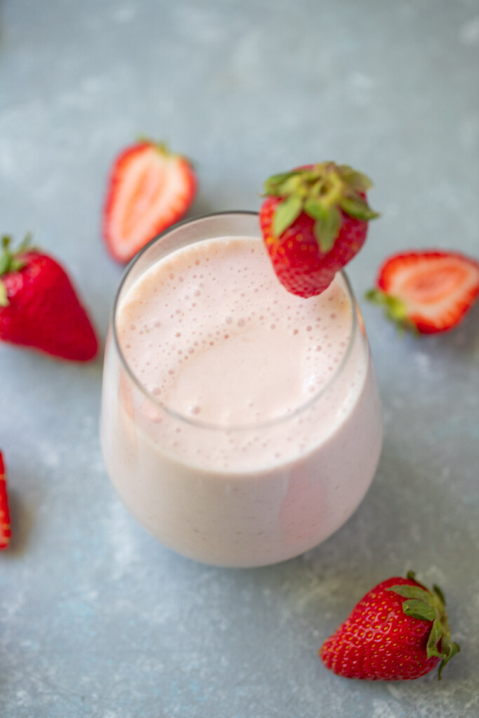 An overhead shot of a smoothie with strawberries in a clear glass with a strawberry on the rim with strawberries in the background