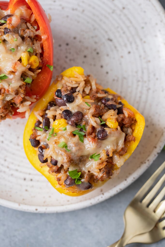 A close up of a white plate with two taco stuffed peppers with two forks on the side