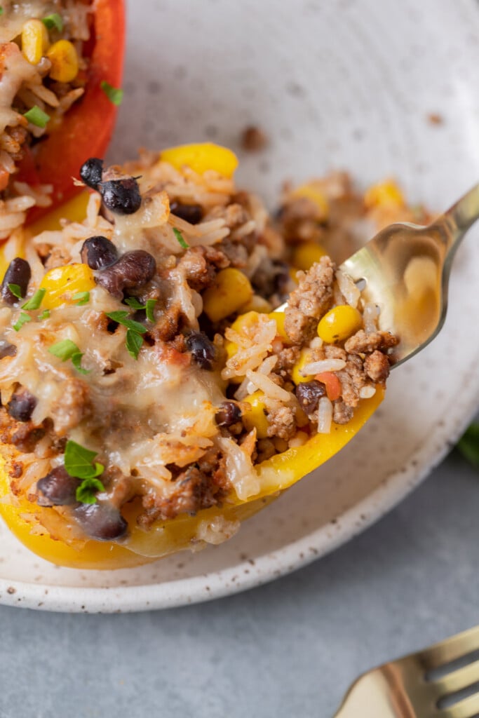 A close up of a fork taking a bite of a taco stuffed pepper on a white plate
