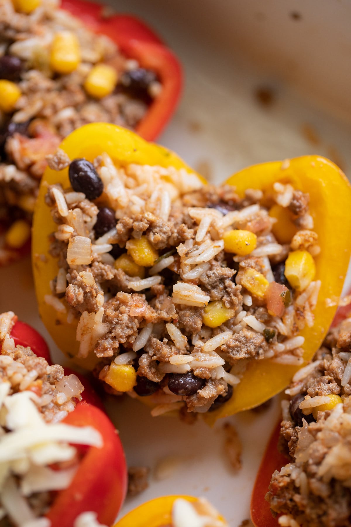 a yellow taco stuffed pepper before being cooked, before being topped with cheese with more halved peppers on the side