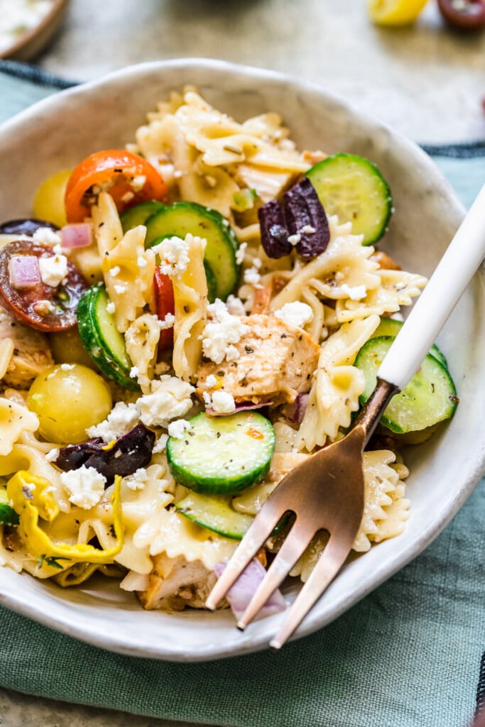 A white plate of greek chicken pasta salad with a fork on the side