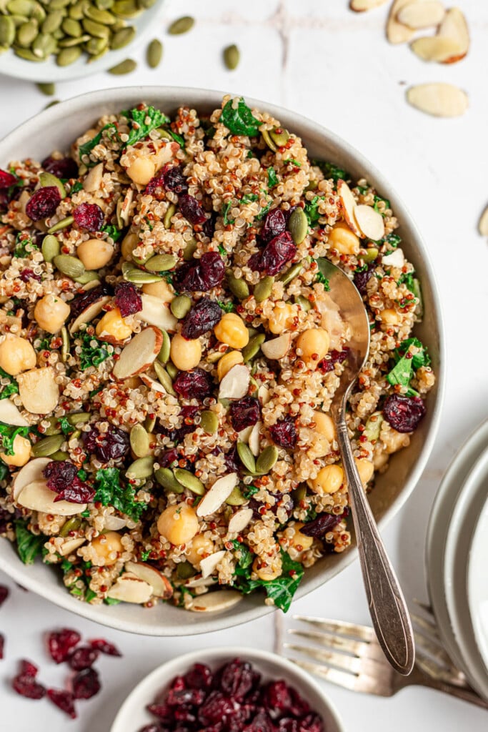 A large bowl of quinoa kale salad with a spoon in it on a white background