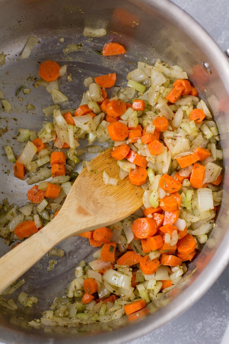 Onions, carrots, garlic, celery sautéed in an Instant pot with a wooden spoon in it.