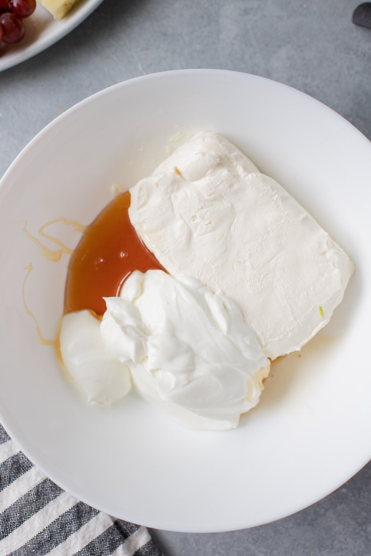 Overhead view of cream cheese, vanilla extract, and Greek yogurt in a white bowl.