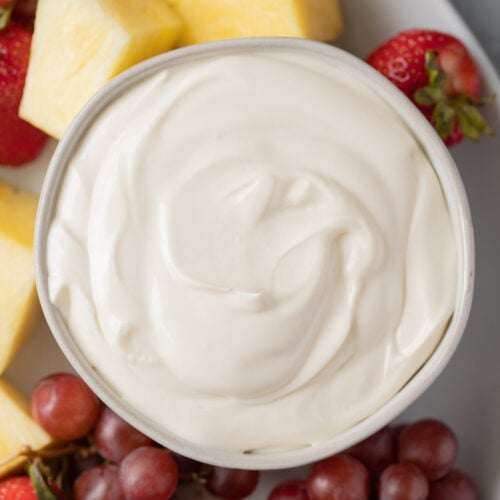 A bowl of healthy fruit dip with grapes, strawberries and pineapple on the side