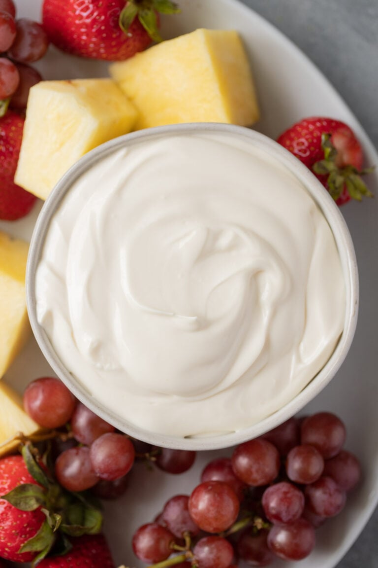 A bowl of healthy fruit dip with grapes, strawberries and pineapple on the side