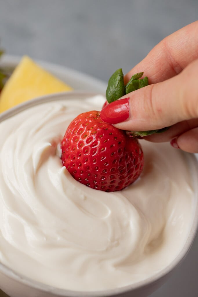 A fresh strawberry being dunked in a bowl of healthy fruit dip.