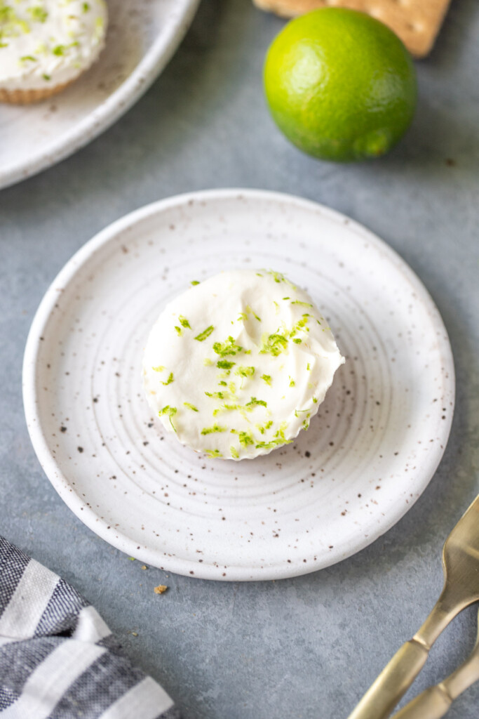 A white plate with one mini lime cheesecake on a grey background with a lime on the side