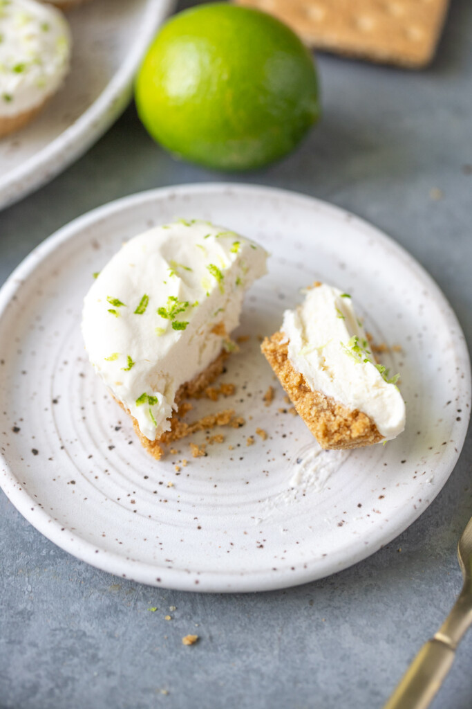 A plate with one mini lime cheesecake cut in half with a lime in the background