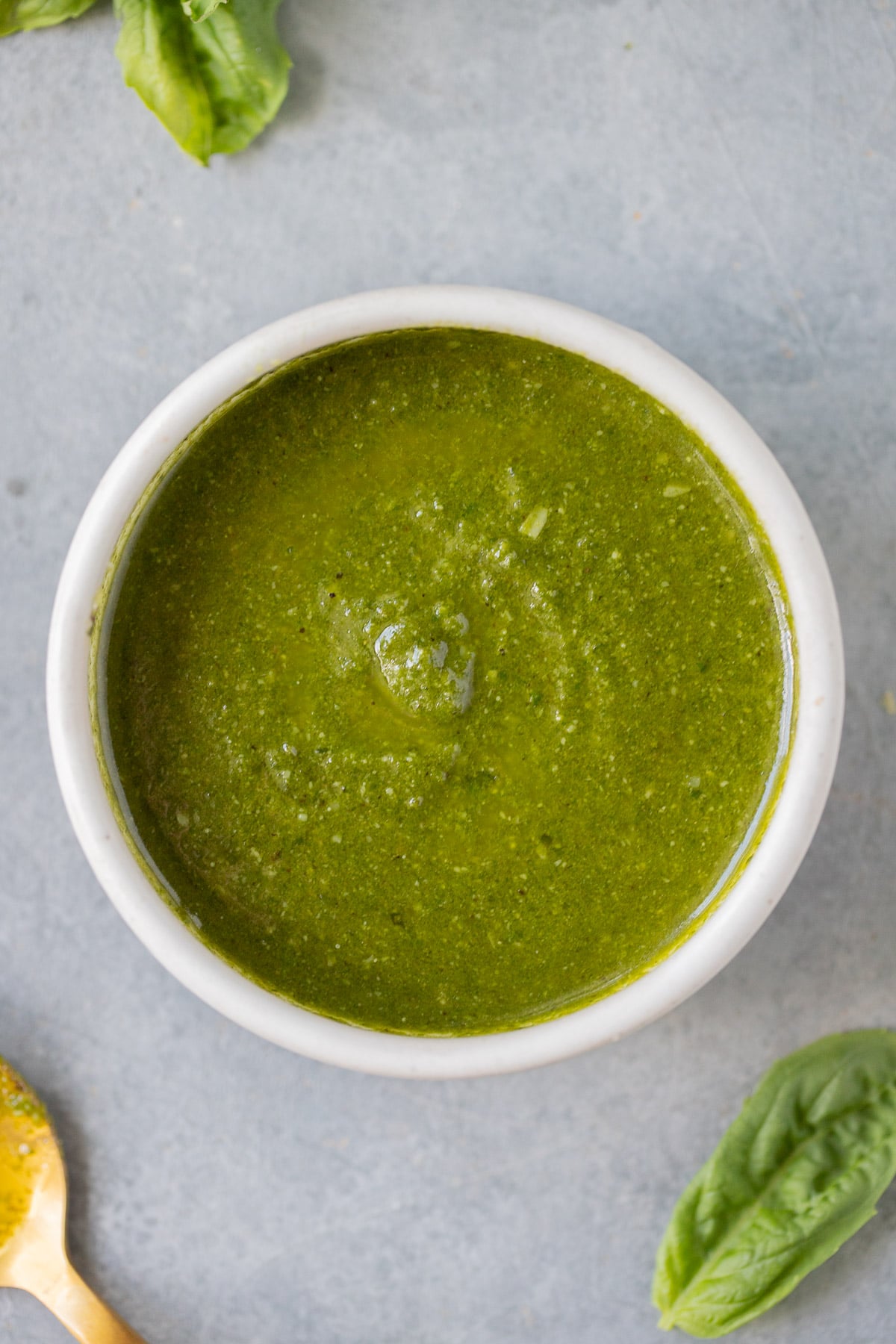 An overhead shot of a white bowl of nut free pesto on a grey background